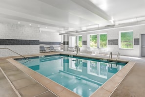 A large indoor swimming pool with clear water, surrounded by lounge chairs and a stone wall.