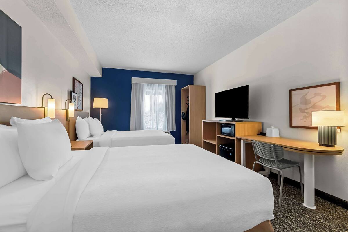 A hotel room with two beds, a desk with a chair, a television, and a window with curtains.