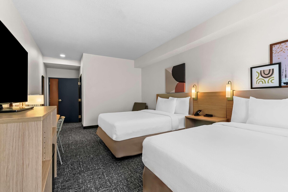 A hotel room with two beds, a desk, a TV, and a door leading to another room.