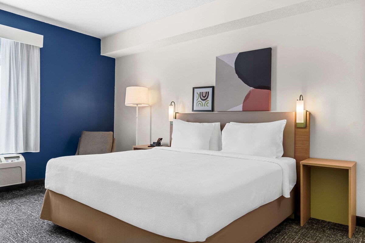 A hotel room with a bed, bedside lamps, a wall-mounted artwork, and a window with curtains.