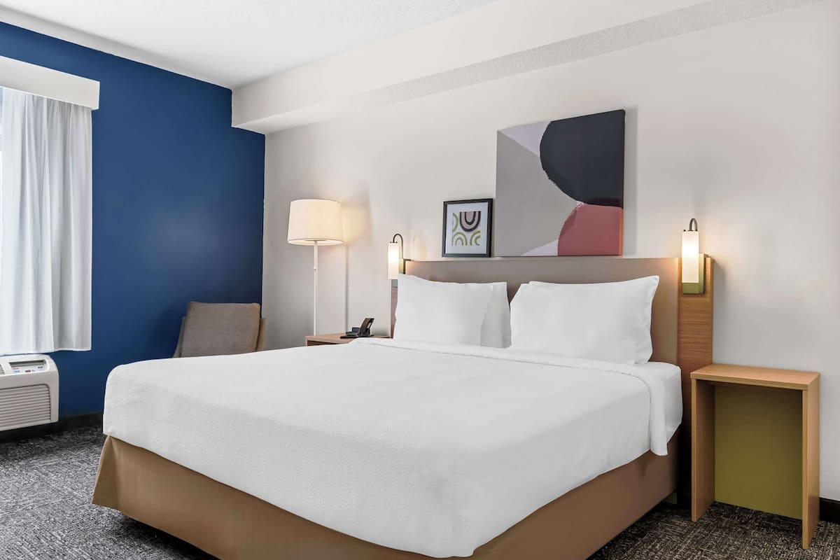 A hotel room with a large bed, bedside tables, a lamp, a wall-mounted artwork, and a window with curtains.