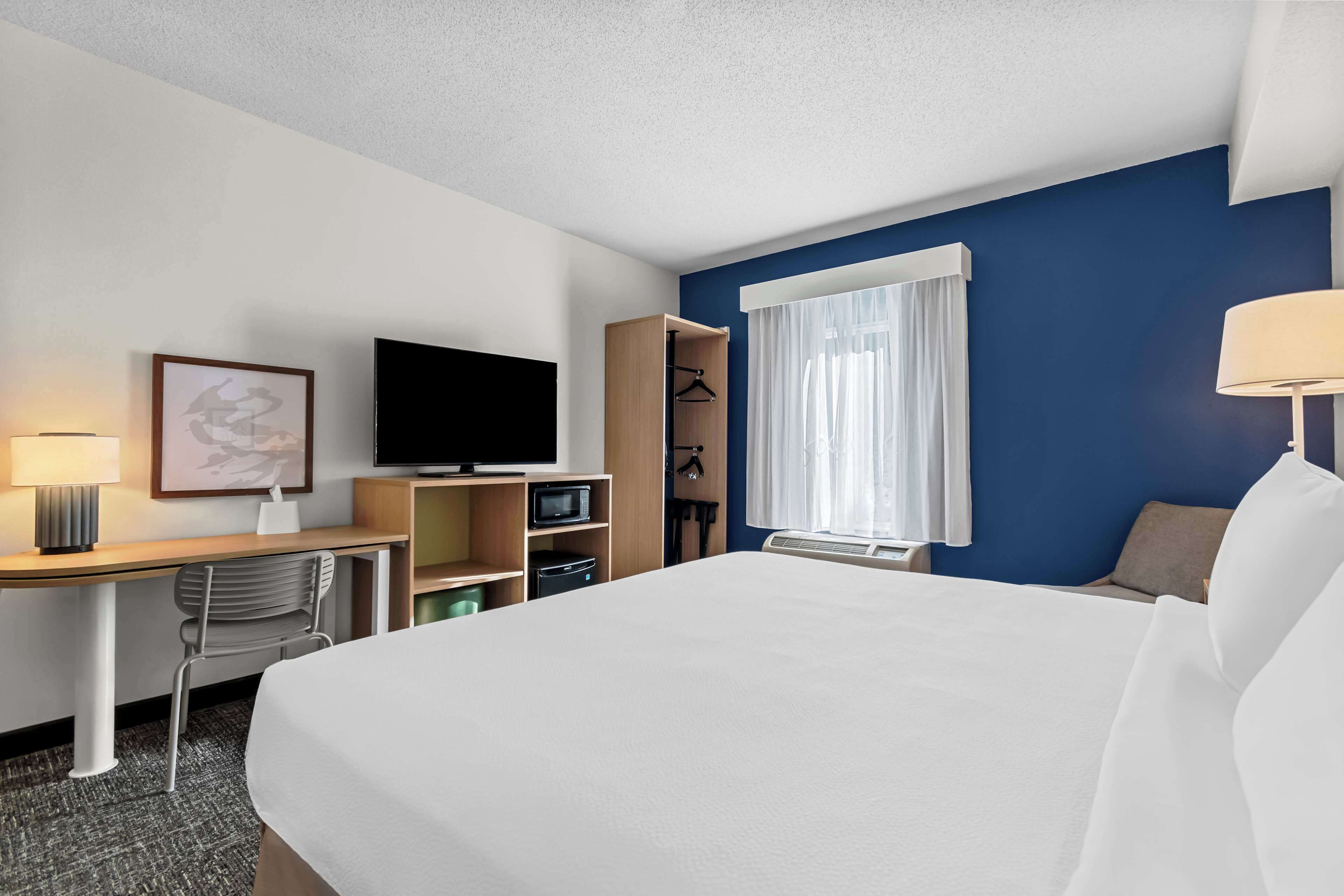 Una camera d'albergo con un letto, una scrivania, una televisione, un armadio e una finestra con tende.