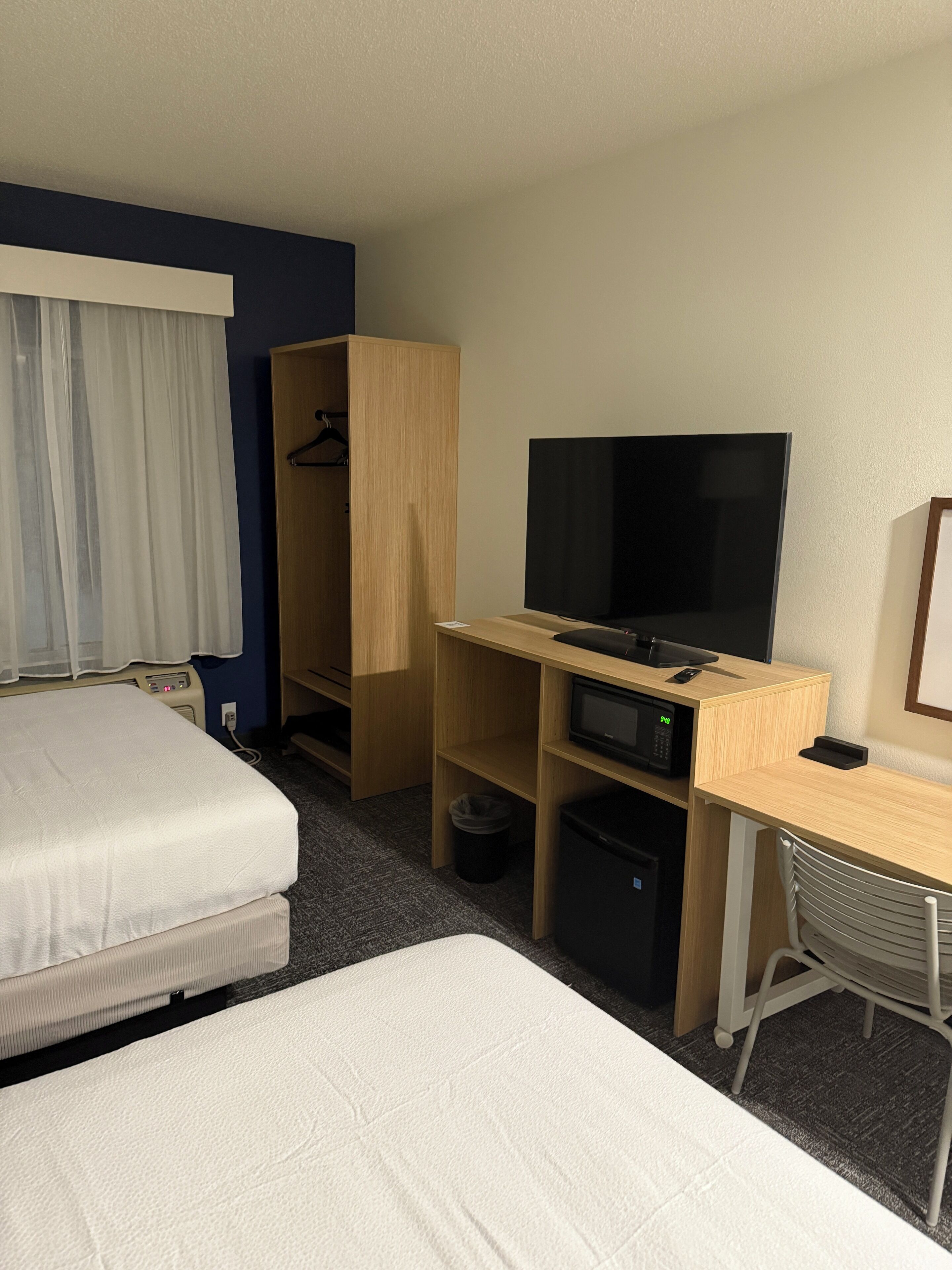 Ein Hotelzimmer mit zwei Betten, einem Fernseher, einem Schreibtisch mit Computer, einer Mikrowelle und einem Kleiderschrank.