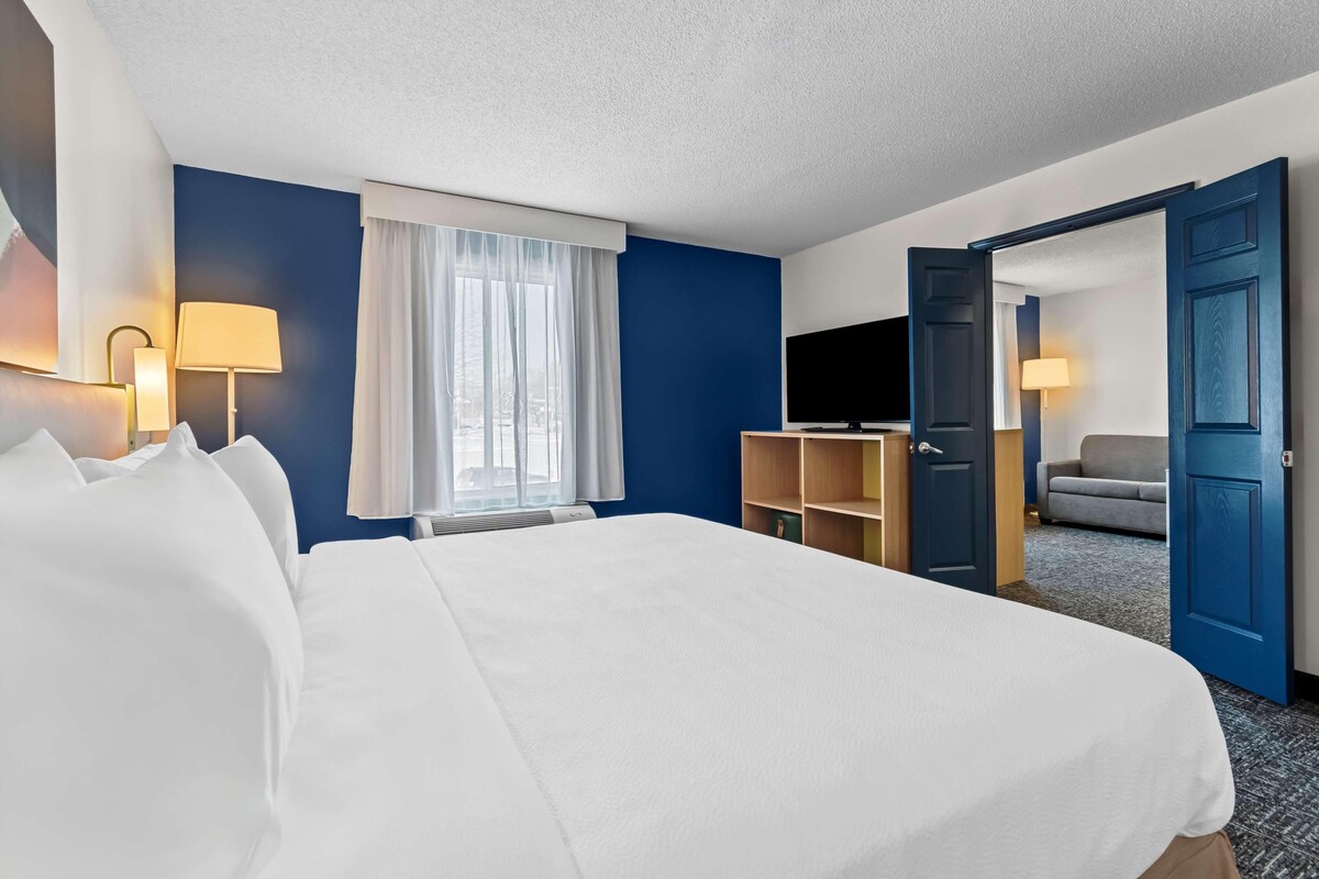 A hotel room with a bed, a TV, a desk, a chair, and a door leading to another room.