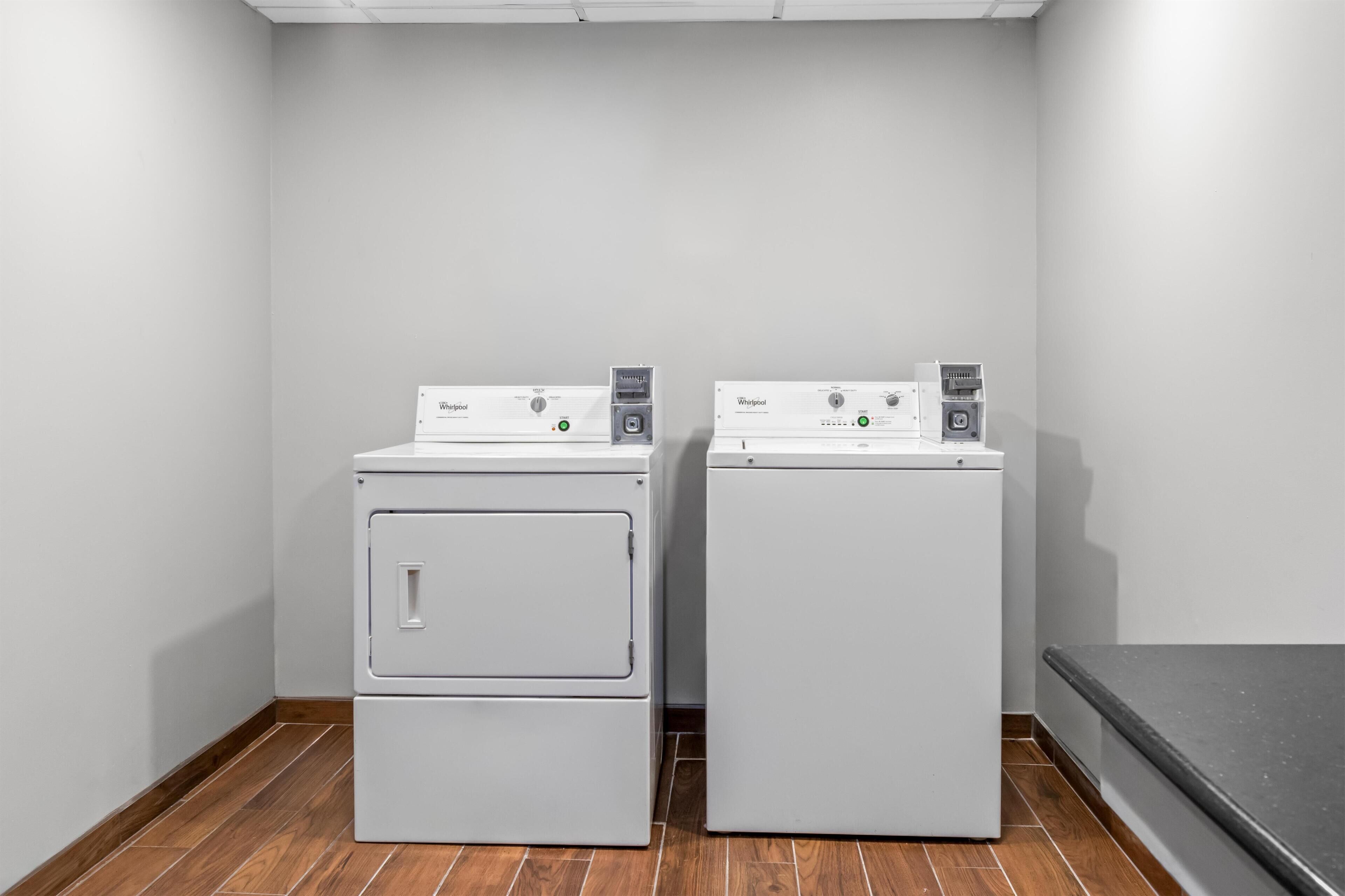 Two white Whirlpool front-loading washing machines in a laundry room with wooden flooring and a grey wall.