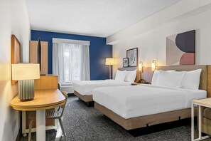 Una habitación de hotel con dos camas, un escritorio, una silla, una lámpara y un ventanal con cortinas.