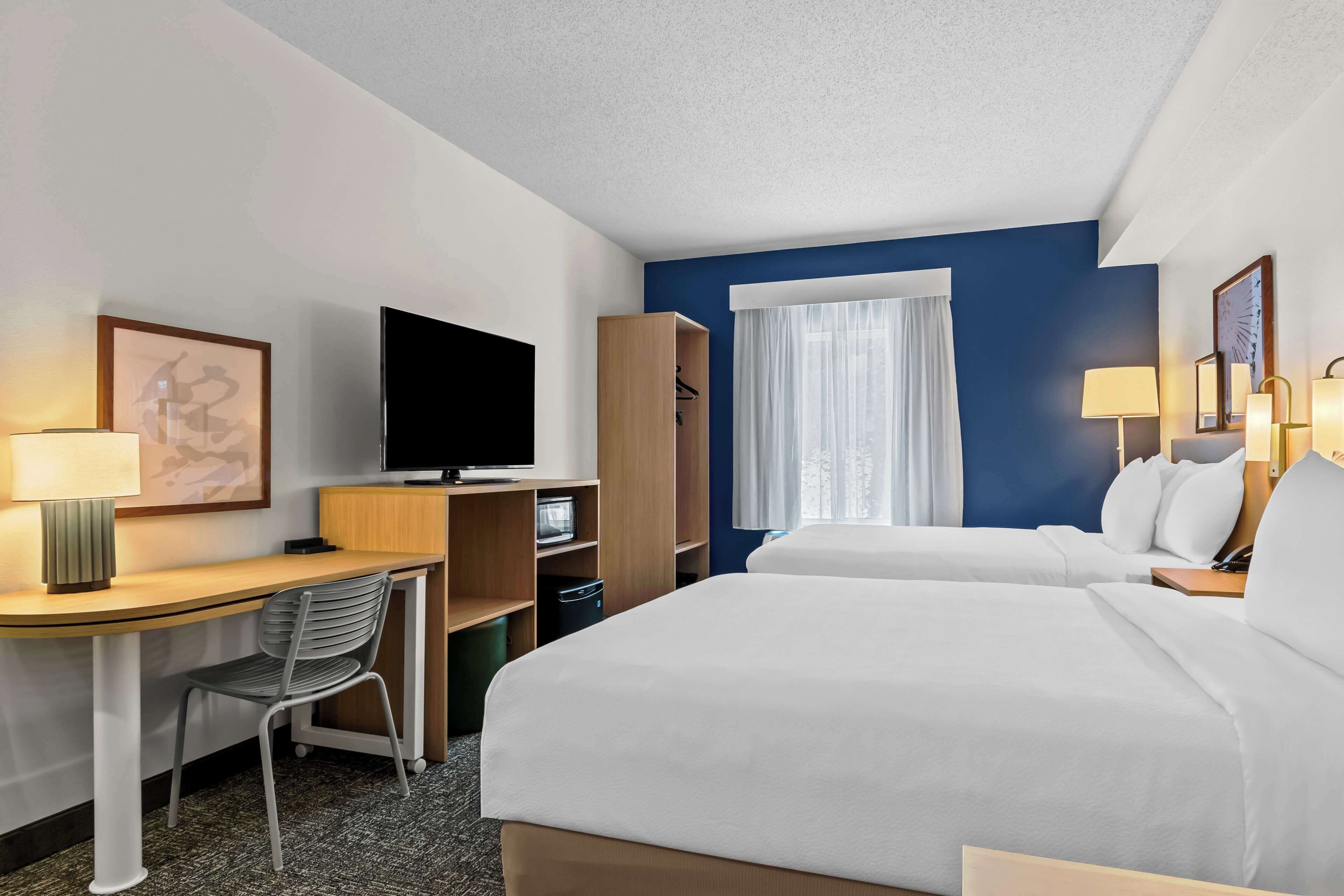 A hotel room with two beds, a desk with a chair, a TV, a wardrobe, and a window with curtains.