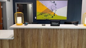 Un mostrador de recepción de hotel con diseño moderno, un cuadro abstracto de gran tamaño y un cartel que indica 'Hilton Honors'.