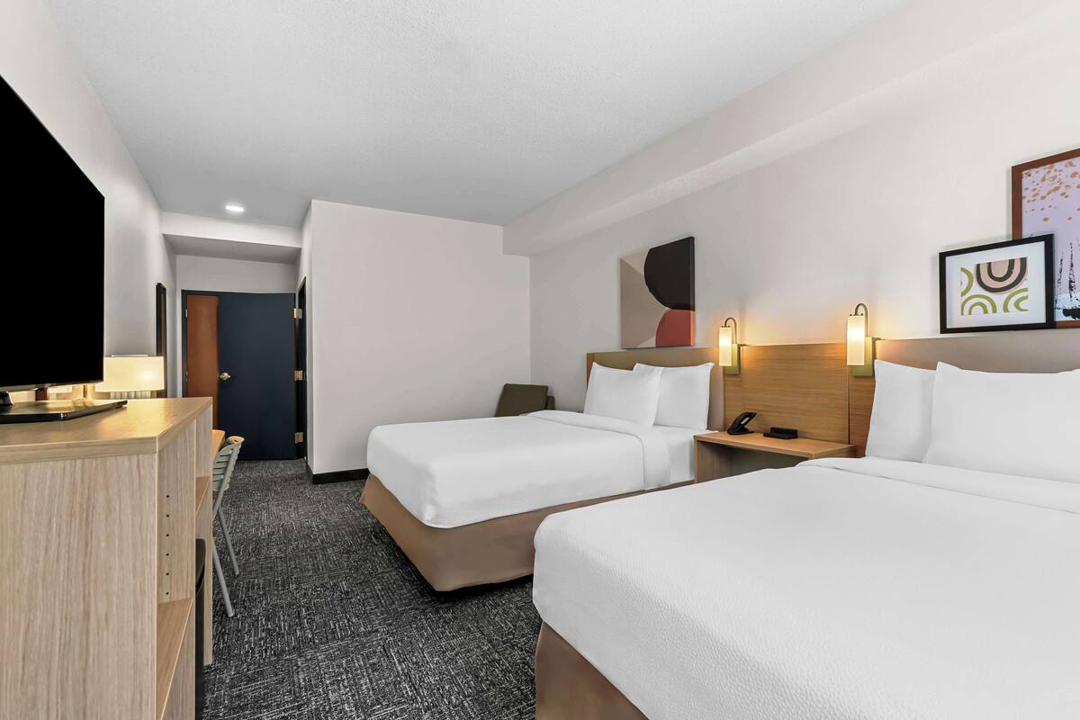 A hotel room with two beds, a desk, a TV, and a door leading to another room.