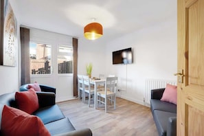 A modern living room with a sofa, a dining table, chairs, a TV, and a wooden door.