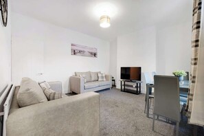 A modern living room with a sofa, a TV, and a dining area with chairs and a table. - Perfect 4BR for Large Groups Sleeps 7 in Stanley (Annfield Plain)