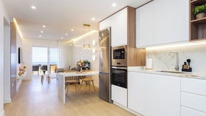 A modern kitchen with white cabinetry, stainless steel appliances, and a wooden dining area. - Home2Book Costa Adeje Escape & Pool, Only Adults (Adeje)