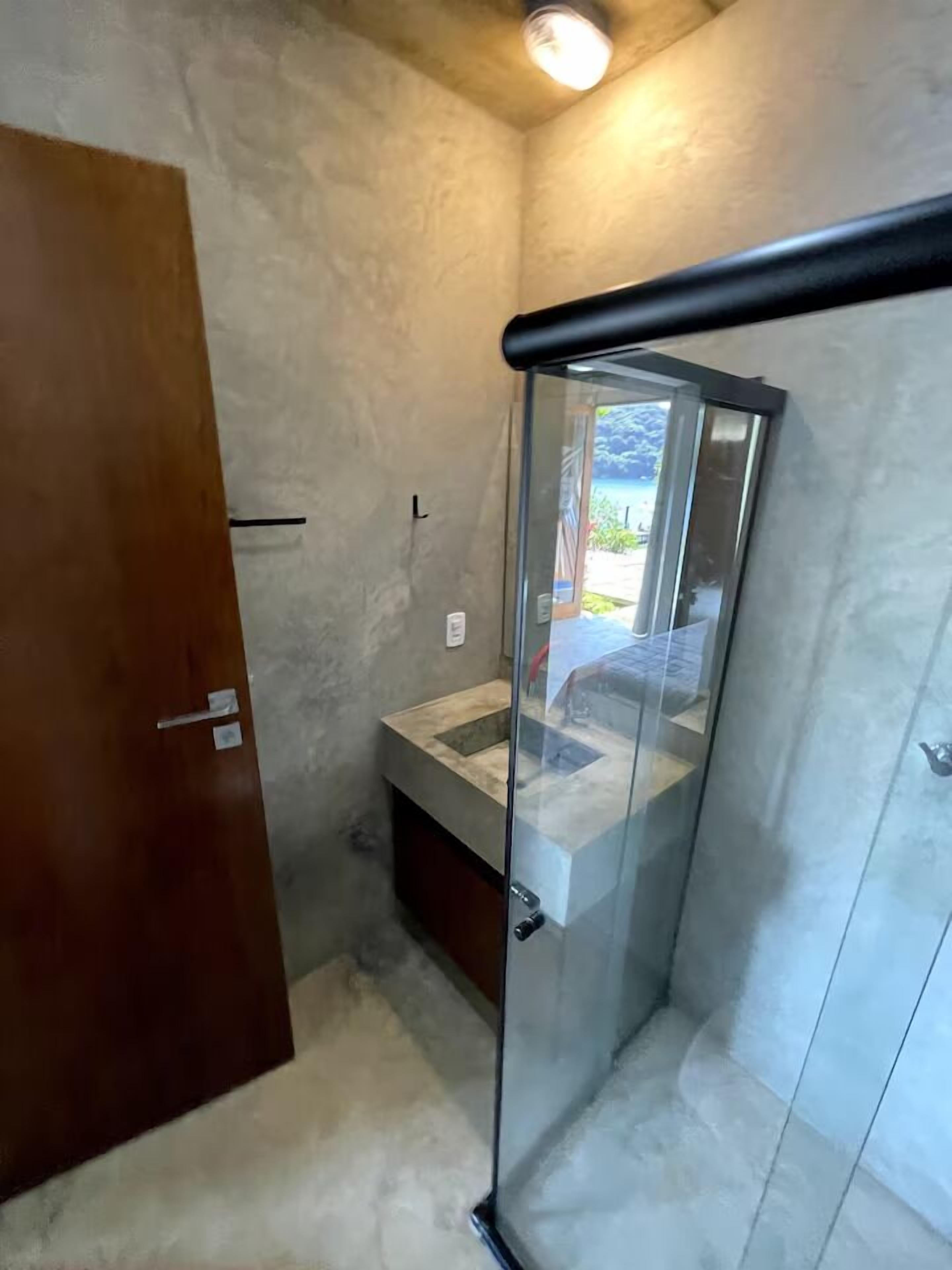 Un baño con cabina de ducha de vidrio, puerta de madera y un ventanal pequeño.