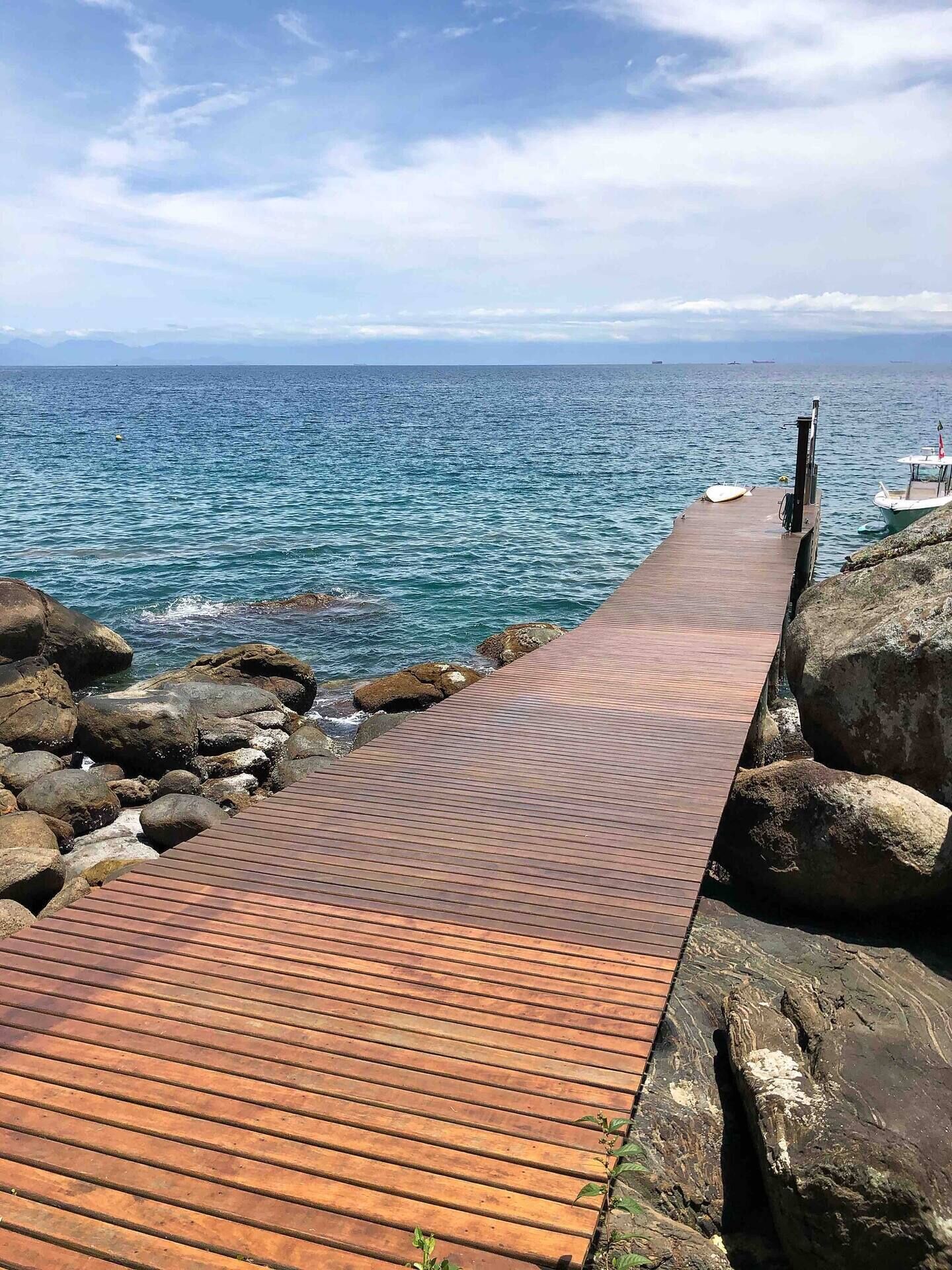 A wooden pier extending into the sea with large rocks on one side and a boat docked on the other.
