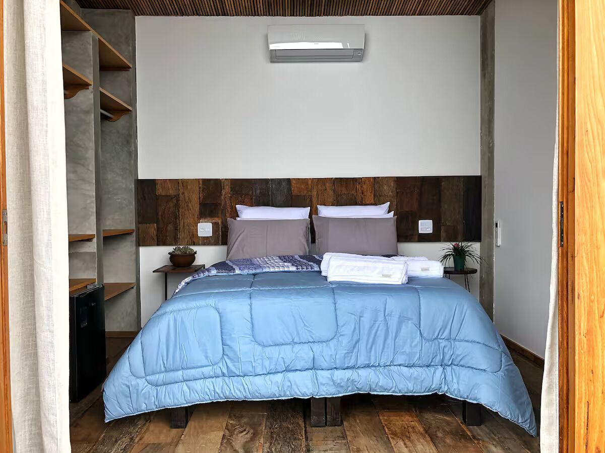 Une chambre à coucher avec un lit, des oreillers, une table de chevet, une petite plante et un climatiseur fixé au mur.