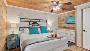 A bedroom with a wooden ceiling, a bed with a white comforter, blue pillows, and a tray with mugs.