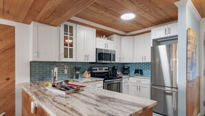 A modern kitchen with white cabinets, a stainless steel refrigerator, a microwave, and a stove.