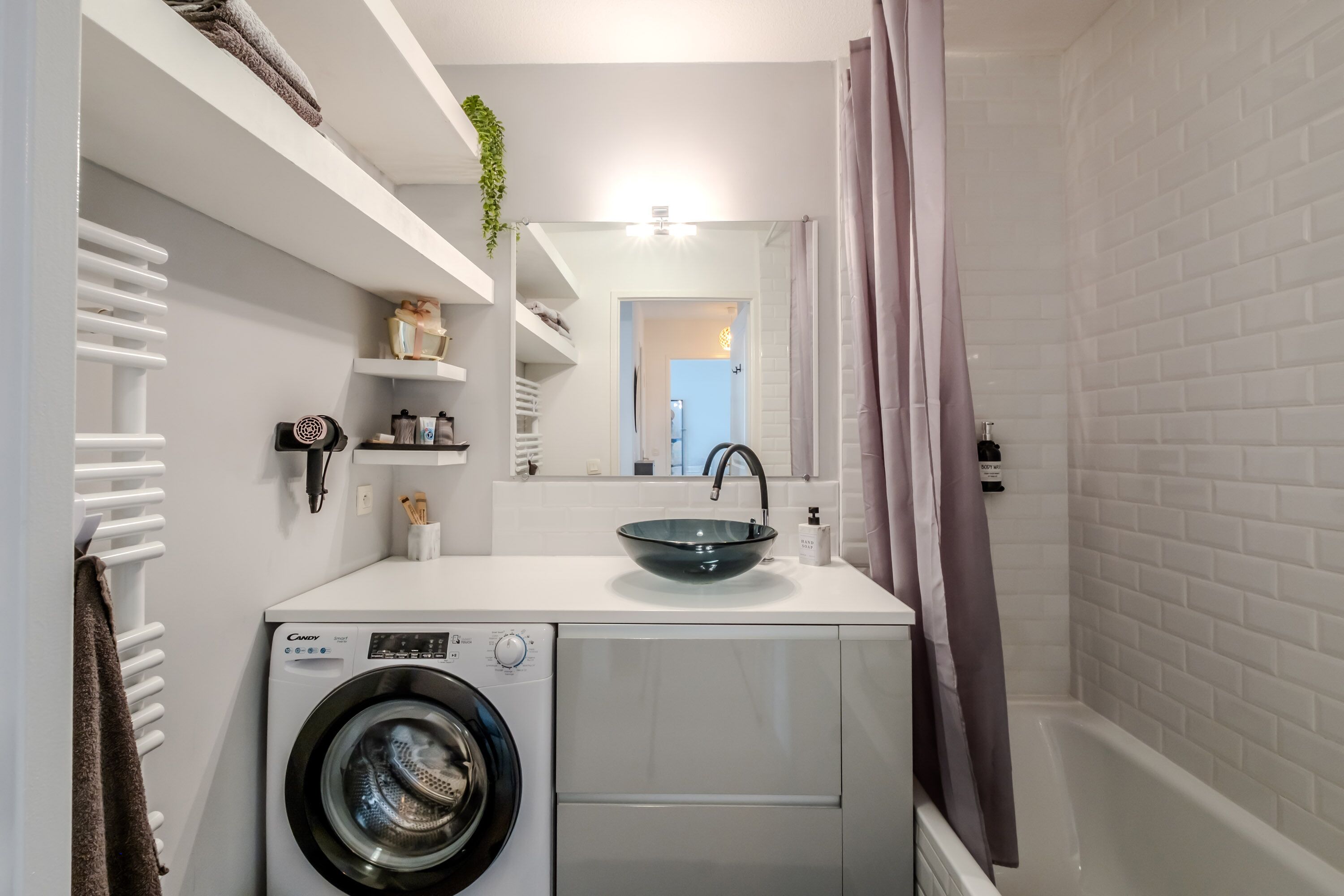 A compact laundry area with a front-loading washing machine, a sink with a glass basin, and a mirror above the counter.