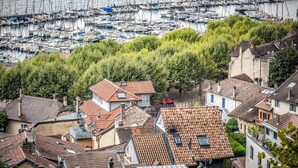 Un puerto deportivo con numerosas embarcaciones amarradas, rodeado de edificios residenciales con tejados de tejas rojas y abundante vegetación.
