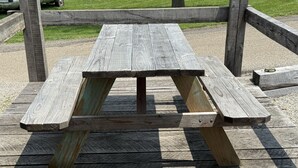 A wooden picnic table with a simple design, supported by wooden posts, set on a wooden deck.