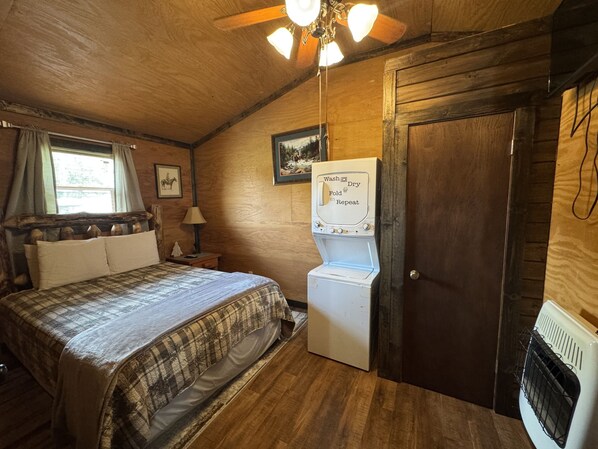 A bedroom with a bed, a washing machine, a wooden door, and a ceiling fan.