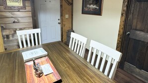 A wooden dining table with white chairs, a framed picture on the wall, and a door with a star decoration.