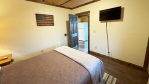 A bedroom with a bed, a ceiling fan, a television mounted on the wall, and a door leading to another room.