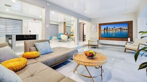 Un salon moderne comprenant un canapé, des fauteuils, un téléviseur et un coin repas avec une table et des chaises.