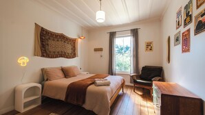 A bedroom with a bed, bedside table, chair, and a window with curtains.