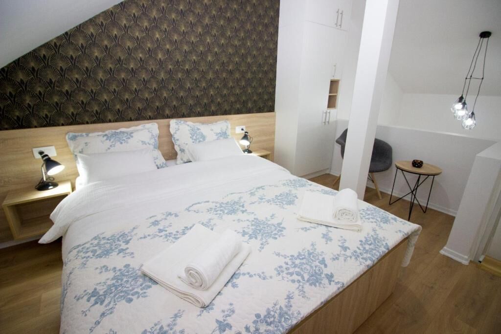 A neatly made bed with a floral bedspread, two bedside lamps, and a small round table with a chair.