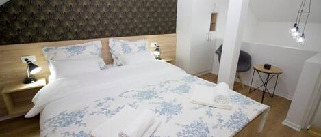 A neatly made bed with a floral bedspread, two bedside lamps, and a small round table with a chair.