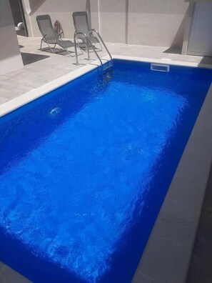 A rectangular swimming pool with clear blue water, surrounded by a tiled deck and two lounge chairs. - Villa Diamond (Mostar)