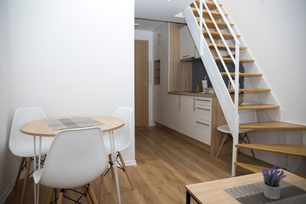 Une cuisine moderne avec des meubles blancs, un escalier en bois et un coin repas comprenant une table et des chaises.
