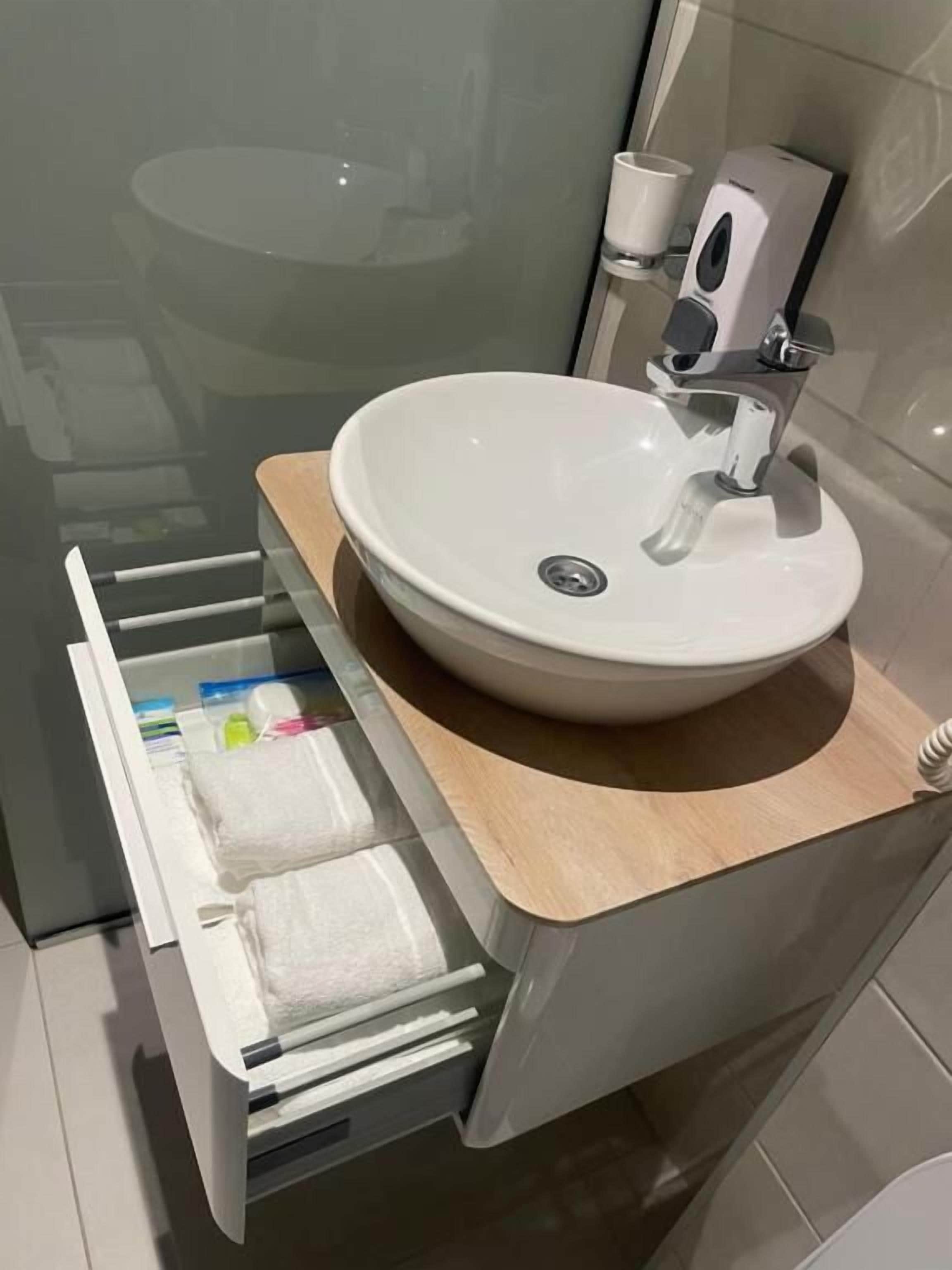 A modern bathroom with a white sink, a wooden countertop, and a towel rack with folded towels.