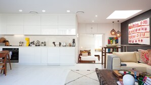 Une cuisine moderne avec des meubles blancs, un coin repas doté d’une table en bois et un salon avec un canapé et une table basse.