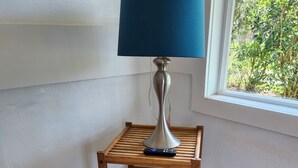 A corner table with a lamp, remote control, and a blue plate. - Yonegan Maui Getaways - Haiku - Unit 7 (Haiku-Pauwela)