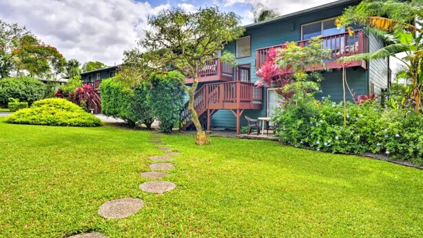 A house with a well-maintained lawn, a wooden deck, and a staircase leading to a balcony. - Yonegan Maui Getaways - Haiku - Unit 7 (Haiku-Pauwela)