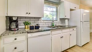 A modern kitchen with white cabinets, a granite countertop, a coffee maker, a sink, and a refrigerator. - The Temple Retreat (Temple)