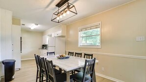 A dining area with a marble table, six chairs, a black trash bin, and a window with blinds. - The Temple Retreat (Temple)