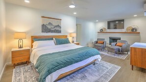A modern bedroom with a large bed, bedside tables, a ceiling fan, a mounted TV, and a fireplace. - Spacious & Stocked: 2Kings+Hot Tub+Fire Pit+Family Fun (Albuquerque)