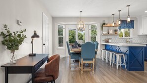 A modern kitchen with a central island, wooden flooring, and a dining area with blue chairs.