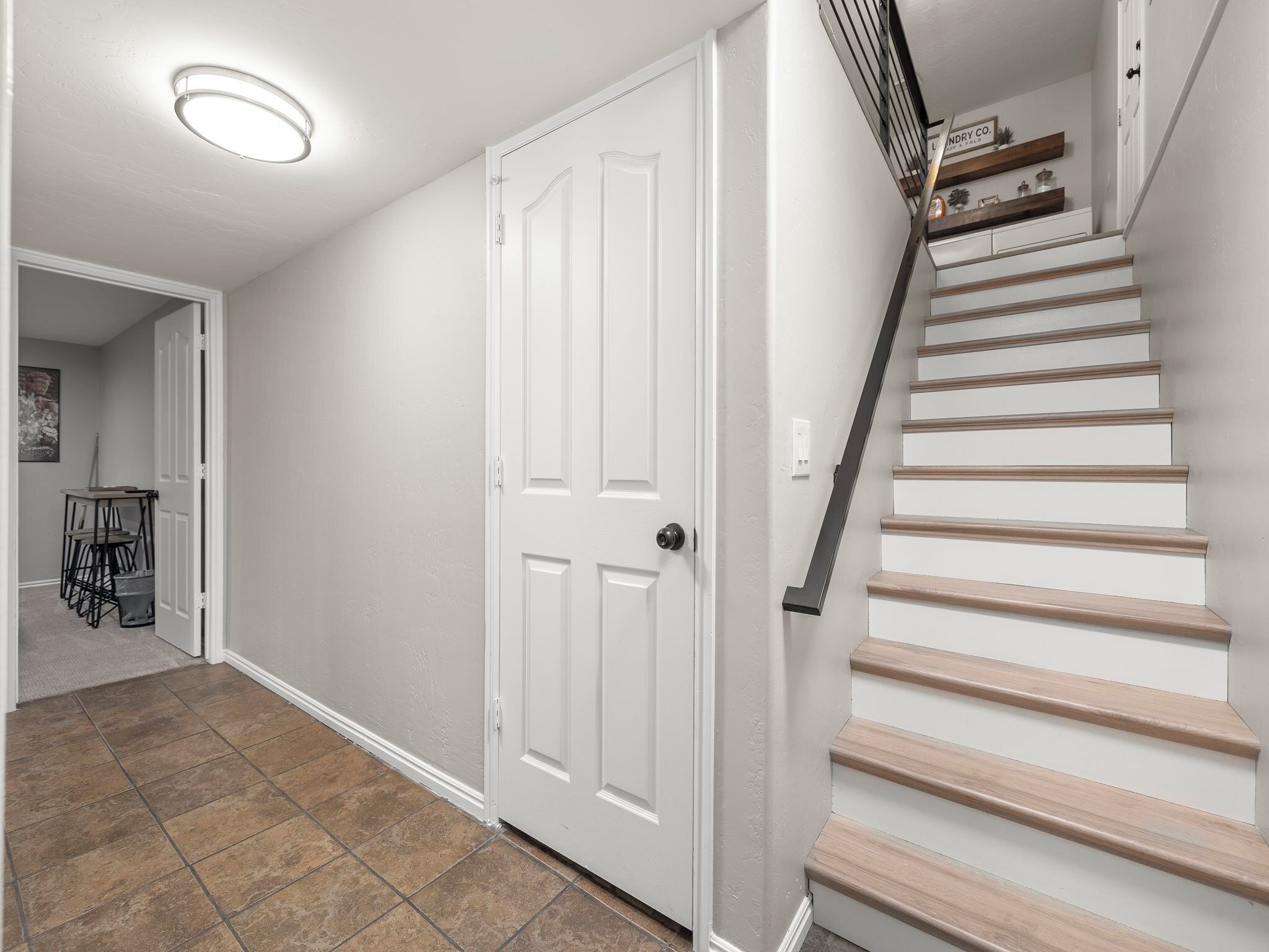 A clean, modern hallway with a white door, a staircase with wooden steps, and a tiled floor.
