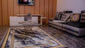 Ein modernes Wohnzimmer mit einer Holzvertäfelung, einem Wand-Fernseher, einer weißen Unterhaltungseinheit, einem runden Couchtisch, einem gemusterten Sofa und einem dekorativen Teppich.