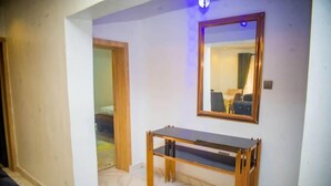 Ein Hotelzimmer mit einem Holztischchen, einem großen Spiegel und einer Tür zu einem weiteren Raum.