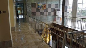 Ein Hotelgang mit Marmorboden, einer Treppe mit Metallgeländern und einer Wand mit einem Gemälde.