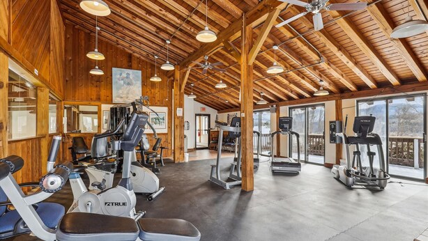 Une salle de sport équipée de divers appareils d’exercice, avec des poutres en bois au plafond et de grandes fenêtres.