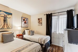 Une chambre d’hôtel avec deux lits, une télévision, une lampe et des œuvres d’art sur le thème du ski accrochées au mur.