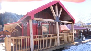 Uma cabana de madeira com telhado vermelho e um deck de madeira, rodeada por neve.