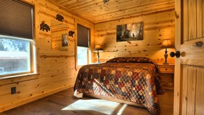 Um quarto aconchegante estilo cabana, com colcha acolchoada, paredes de madeira, uma janela e um quadro na parede.