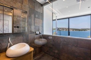 Une salle de bain moderne avec une grande fenêtre, des murs en pierre et un lavabo blanc.